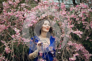 Portrait of a middle-aged brunette in a blue dress next to a cherry blossom