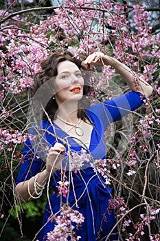 Portrait of a middle-aged brunette in a blue dress next to a cherry blossom