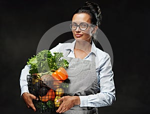 Portrait of a middle-aged female farmer in apron holds a basket of fresh vegetables and fruit