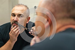 Portrait of Middle-aged handsome man cutting his beard and mooustache with scissors