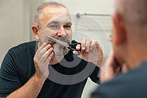 Portrait of Middle-aged handsome man cutting his beard and mooustache with scissors