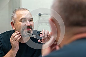 Portrait of Middle-aged handsome man cutting his beard and mooustache with scissors