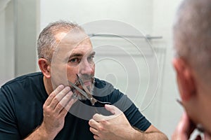 Portrait of Middle-aged handsome man cutting his beard and mooustache with scissors