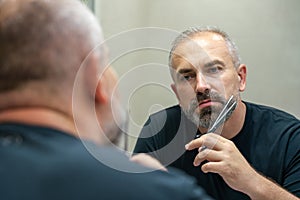 Portrait of Middle-aged handsome man cutting his beard with scissors. Selfcare during quarantine isolation