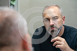 Portrait of Middle-aged handsome man cutting his beard with scissors. Selfcare during quarantine isolation