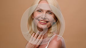 Portrait middle aged happy mature Caucasian woman senior 50s model flirty smiling at camera on beige studio background