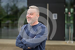 Portrait of a middle aged man looking friendly with a beaming smile to camera with his arms folded