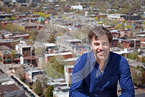 A portrait of a middle-aged man with a short beard smiling on a city background