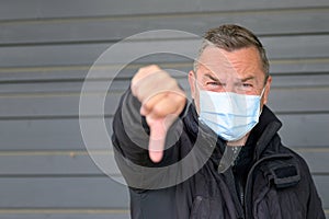 Portrait of a middle-aged man wearing protection mask while showing thumb down