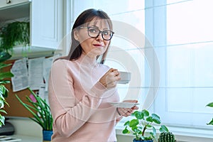 Portrait of middle-aged woman holding cup of coffee looking at camera