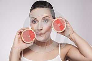 Portrait of middle aged woman with perfect skin smiling after cream, balm, mask, lotion, holding slice grapefruit in her hands and