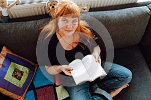 portrait middle-aged woman reading book while sitting on sofa