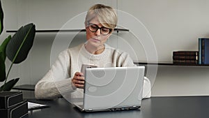 Portrait of a middle-aged woman using a laptop and a smartphone. A woman exchanges text messages while working in the