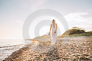 Portrait of middle-aged woman walking on sandy beach near water sea ocean on sunny day, holding straw hat in hands.