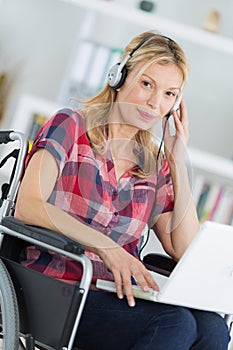 Portrait middle aged woman in wheelchair with laptop and headphones