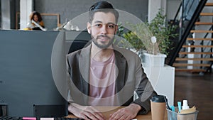 Portrait of Middle Eastern man smiling at computer desk in coworking location