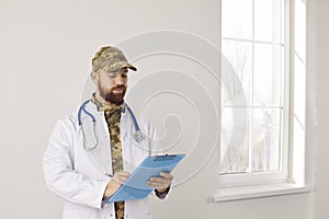 Portrait of military doctor in camouflage uniform and medical lab coat with clipboard
