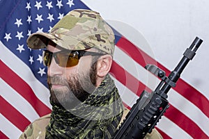 Portrait of a military man 30-35 years old with a rifle on his shoulder, wearing dark glasses against the background of the Americ