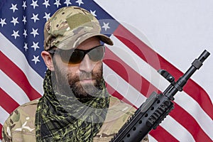 Portrait of a military man 30-35 years old with a rifle on his shoulder, wearing dark glasses against the background of the Americ