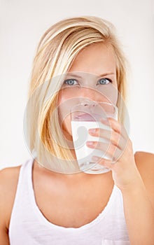 Portrait, milk and a woman drinking from a glass in studio isolated on a white background. Health, nutrition and calcium