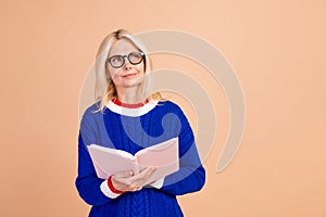 Portrait of minded person with stylish hair wear blue pullover in eyewear hold book look empty space isolated on beige