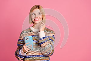 Portrait of minded smart woman dressed knit jumper hold smartphone look at proposition empty space  on pink