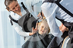 Portrait through mirror of hairdresser make haircut to a boy