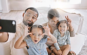 Portrait of a mixed race family taking a selfie and making funny faces while sitting on the sofa at home. Hispanic man