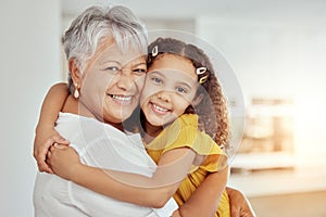 Portrait of mixed race grandmother and granddaughter hugging in living room at home. Smiling hispanic girl embracing