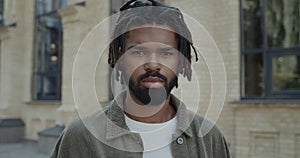 Portrait of mixed race guy with beard looking to camera. Close up view of young serious man with dreadlocks standing at