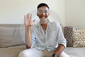 Portrait of mixed race man sitting on sofa looking at camera waving and smiling