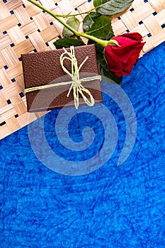 Portrait mode top shot of a brown gift box with one red rose over blue background. Husband gift concept