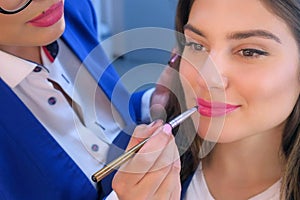 Portrait of model girl on professional makeup, visagiste applying lipstick.