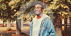 Portrait of modern happy smiling african man looking away wearing eyeglasses in autumn city park on yellow leaves background