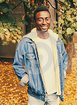 Portrait of modern happy smiling african man looking away wearing eyeglasses in autumn city park on yellow leaves background