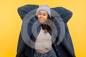 Portrait of modern happy trendy girl wearing warm winter hat and fur coat looking at camera with toothy smile