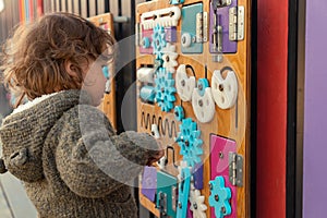 Portrait of a modern little boy playing with a busy board outdoors