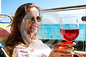 Portrait of modern long hair woman holding in hand a glass of red wine on the background seascape view.