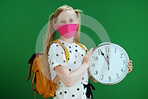 Portrait of modern school girl showing clock isolated on green