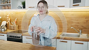 Portrait of modern stylish girl with glasses and blue shirt in kitchen of house, woman in playful mood, laughs and jokes