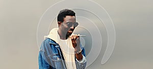 Portrait of modern young african man holding smartphone using voice command recorder, assistant or takes calling, looking at phone