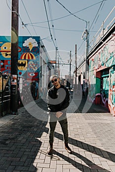 Portrait of Modern Young Person Hipster Guy Standing Alone in Urban Street Covered Colorful Graffiti Alleyway Outside in the City