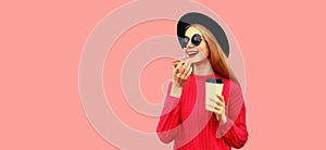 Portrait of modern young woman eating donut drinking coffee isolated on pink background