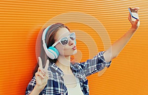 Portrait of modern young woman taking selfie picture by smartphone in wireless headphones listening to music blowing lips