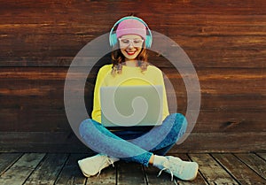 Mladá žena pracovné prenosný počítač načúvanie na hudba v slúchadlá nosenie farbistý oblečenie na drevený 