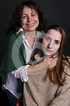 Portrait of mom and adult daughter posing in studio on a black background. Intergenerational concept. Copy space.