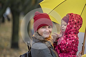Portrait of mom and baby on the hands under yellow umbrella in park. Mother smiles and looking at camera. Autumn walking