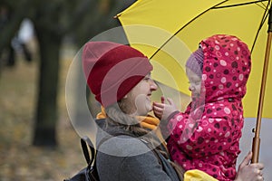 Portrait of mom and baby under yellow umbrella in park. Mom smiles at her daughter