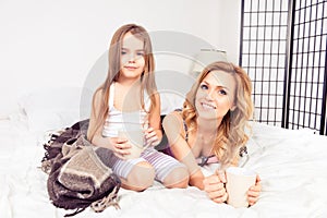 Portrait of mom and daughter lying in bed with cups of hot milk