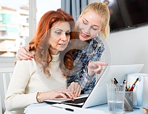Portrait of mom and daughter at table using laptop together